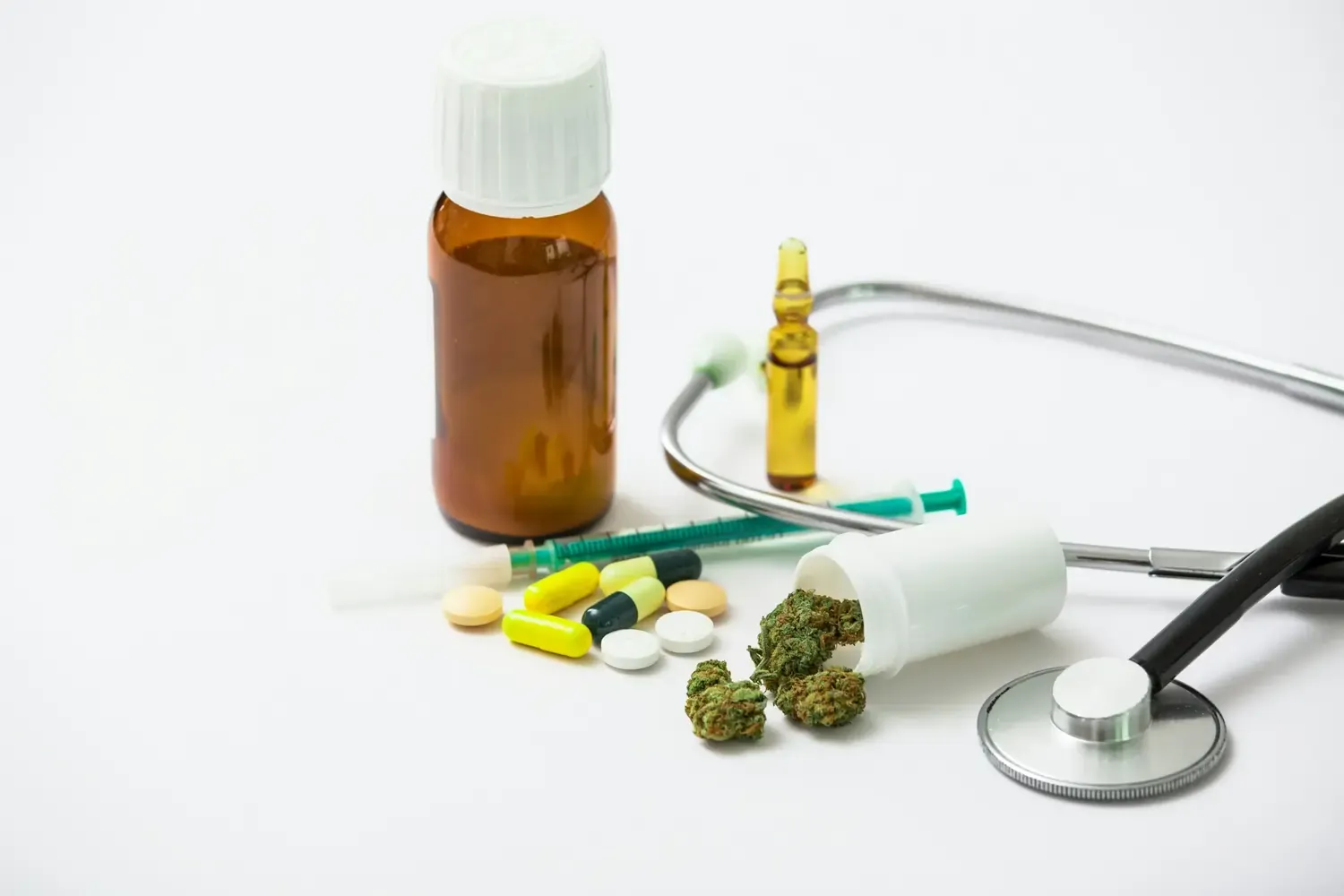 Cannabisblüten neben Pillen, Ampulle, Spritze und Stethoskop auf weißem Hintergrund