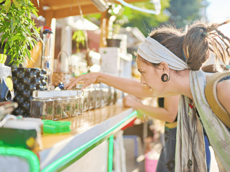 Legaler Verkauf von Cannabis in der Schweiz. Eine Frau mit Dreads schaut sich verschiedene Blüten an einem Verkaufstresen an.