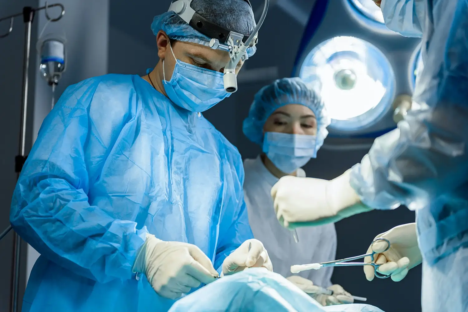 Arzt mit Stirnlampe operiert, Assistent reicht sterile Instrumente