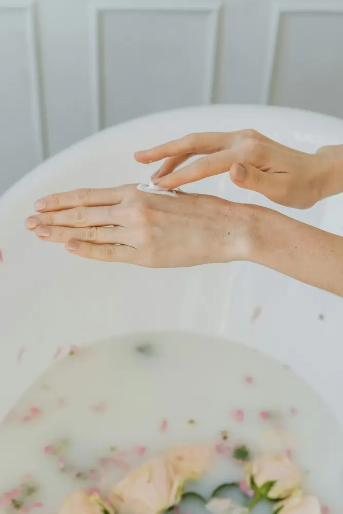 Hände, die Creme auf den Handrücken verteilen über einem Milchbad mit Rosen