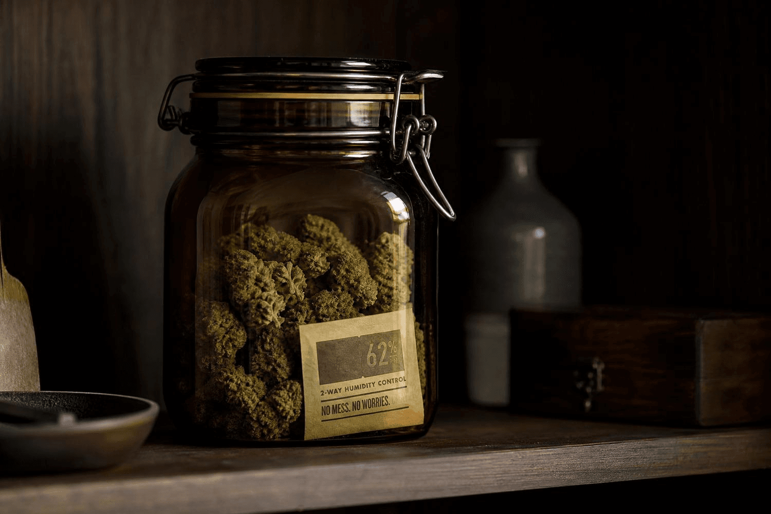 Luftdichtes Braunglas-Bügelglas mit getrockneten Cannabisblüten auf einem Holzregal, mit einem 62%-Humidity-Control-Pack im Inneren – optimale Lagerung zur Aromaerhaltung.