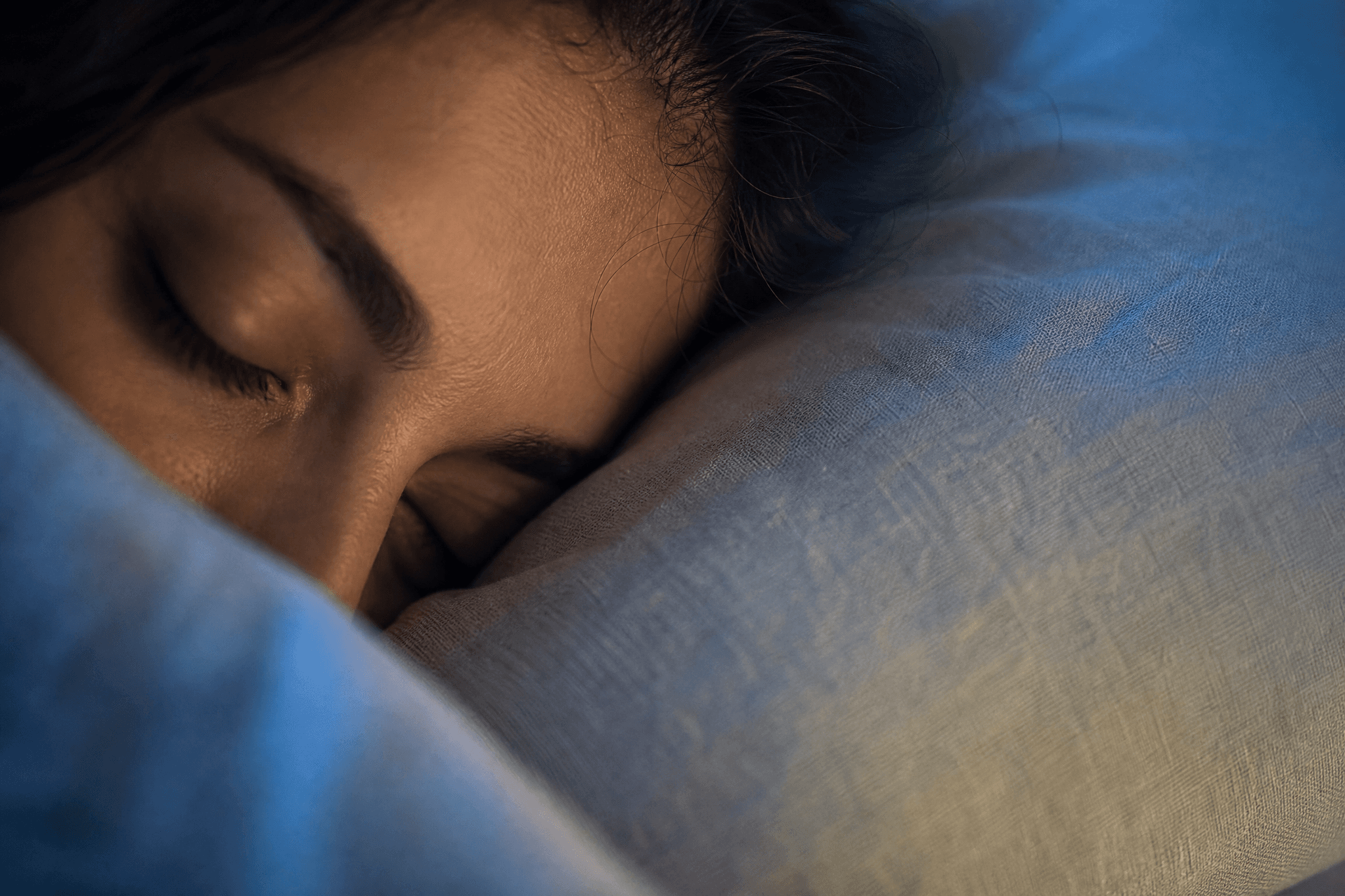 Nahaufnahme einer schlafenden Person mit geschlossenem Auge auf einem Leinenkissen im sanften Nachtlicht.