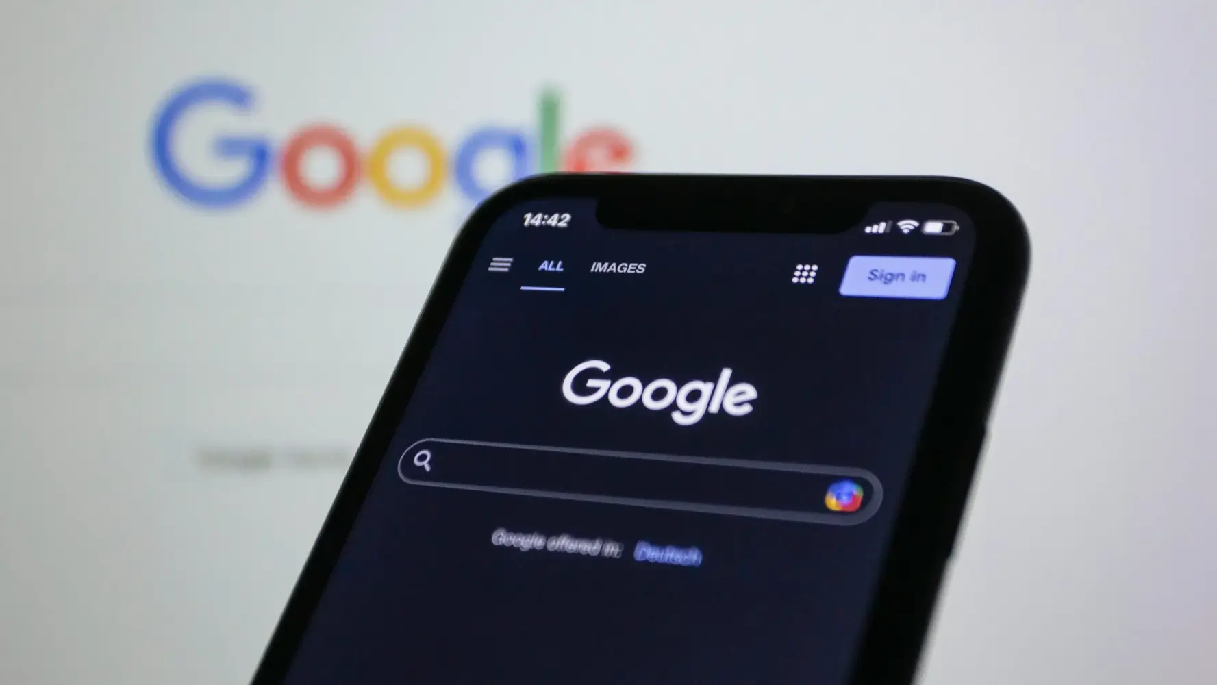 Smartphone zeigt Google-Startseite im Dunkelmodus vor unscharfem Logo