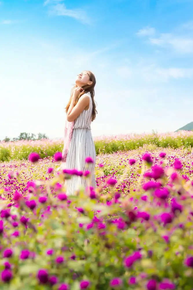 Frau im weißen Kleid in lila Blumenwiese, blickt zum blauen Himmel