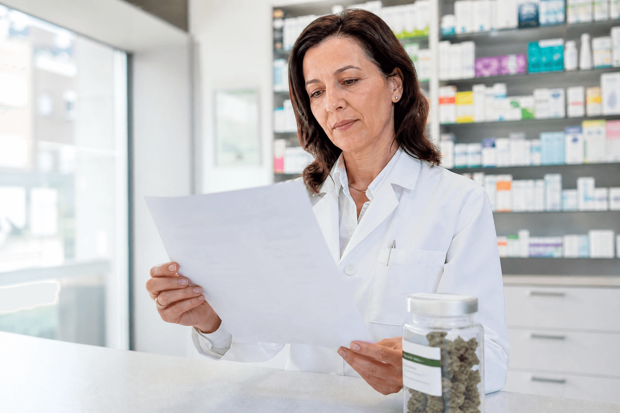 Apothekerin prüft ein Rezept neben einem Glas Cannabisblüten in der Apotheke – Symbolbild zur geplanten Streichung der Erstattung durch die GKV