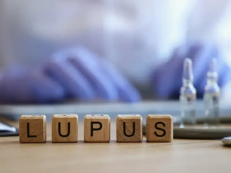 Holzklötze mit LUPUS auf Tisch, medizinische Ampullen im Hintergrund