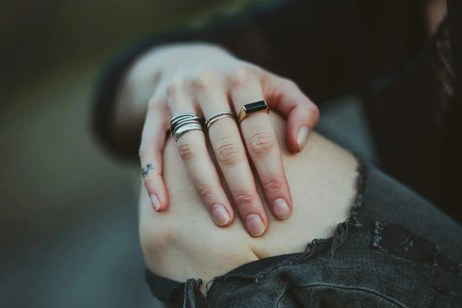 Hand auf Knie mit mehreren Ringen, schwarzem Onyxring und kleinem Tattoo