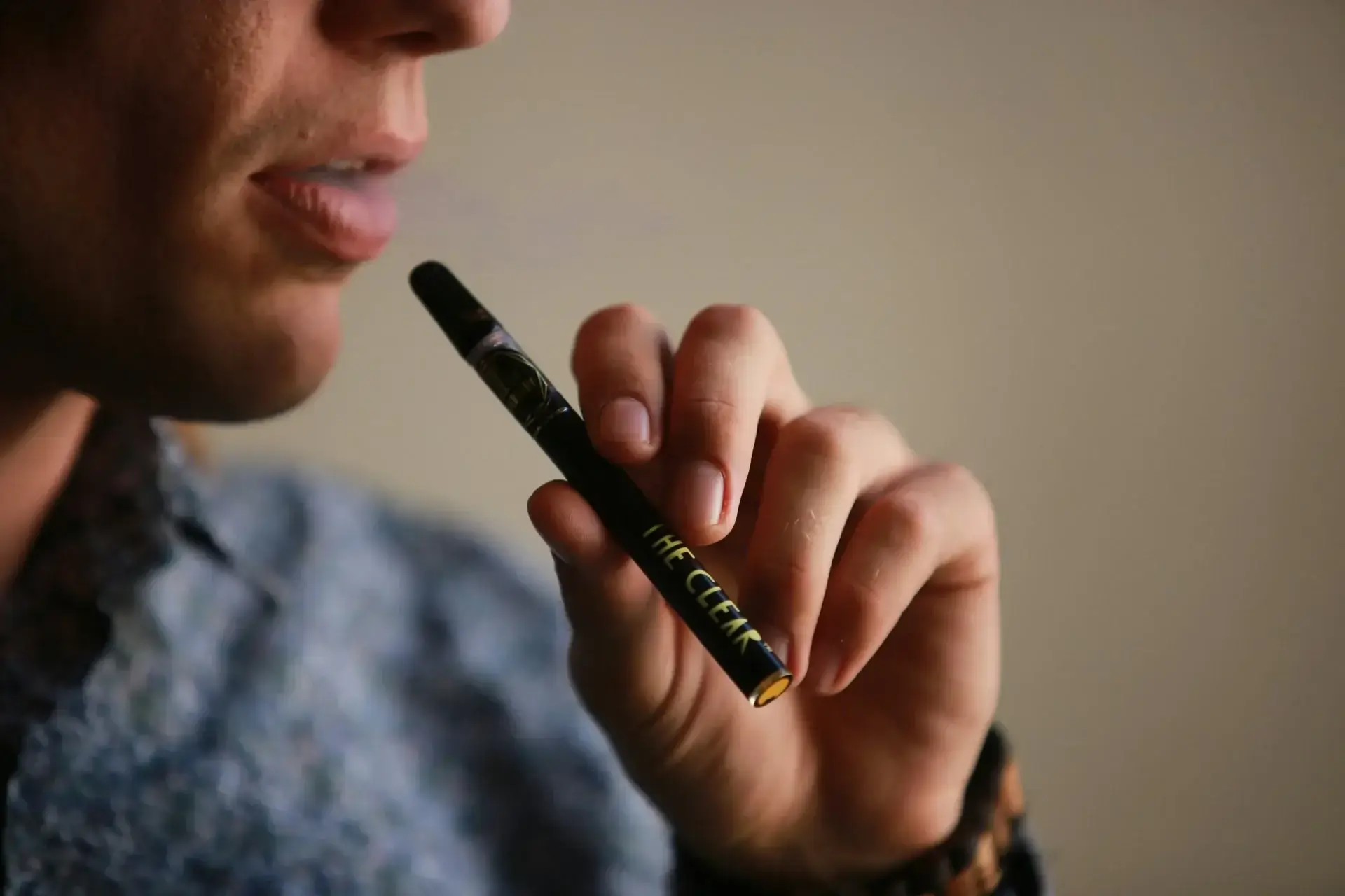 Nahaufnahme: Hand hält Vape-Pen am Mund, leichter Dampf steigt