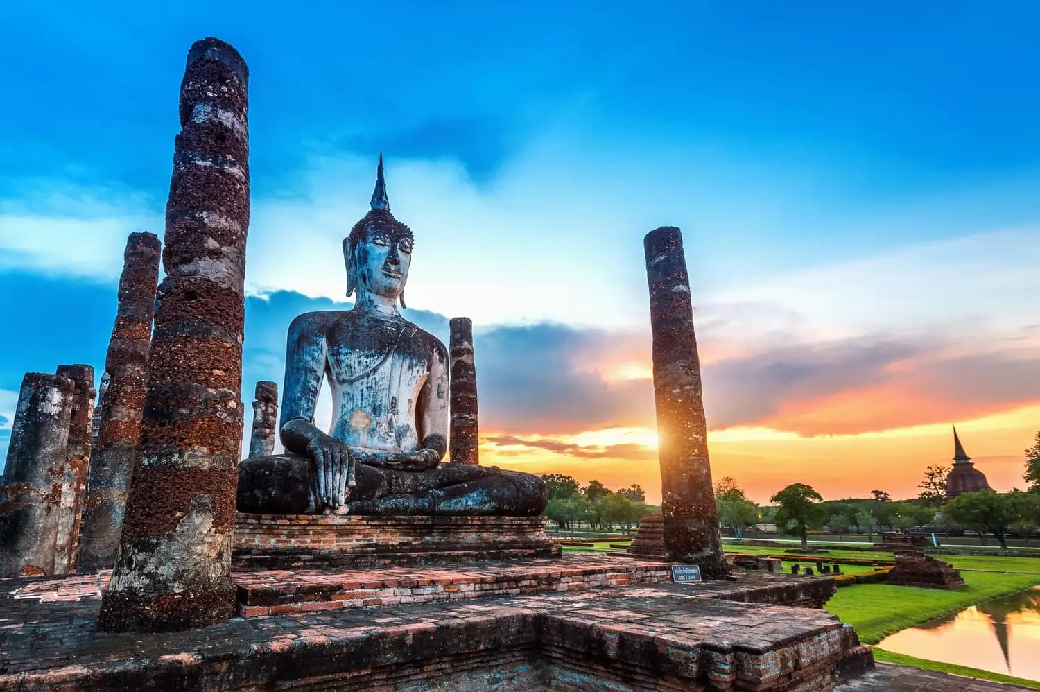 Sitzende Buddha-Statue zwischen verfallenen Säulen im Sonnenuntergang