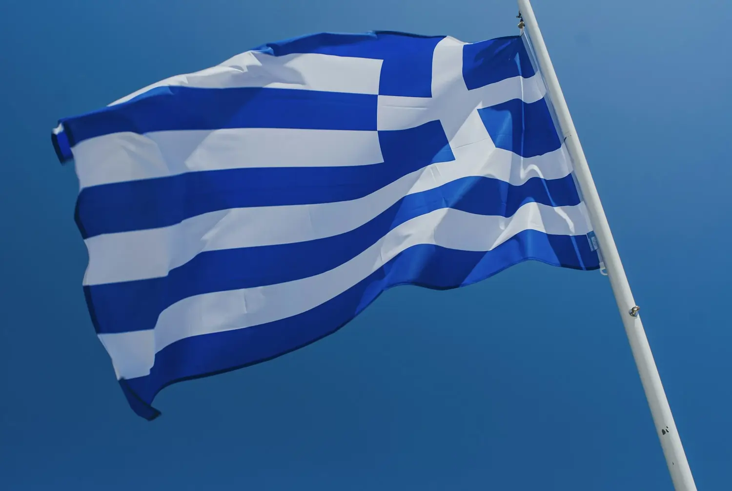 Blau-weiße griechische Flagge am Mast, im Wind vor klarem Himmel