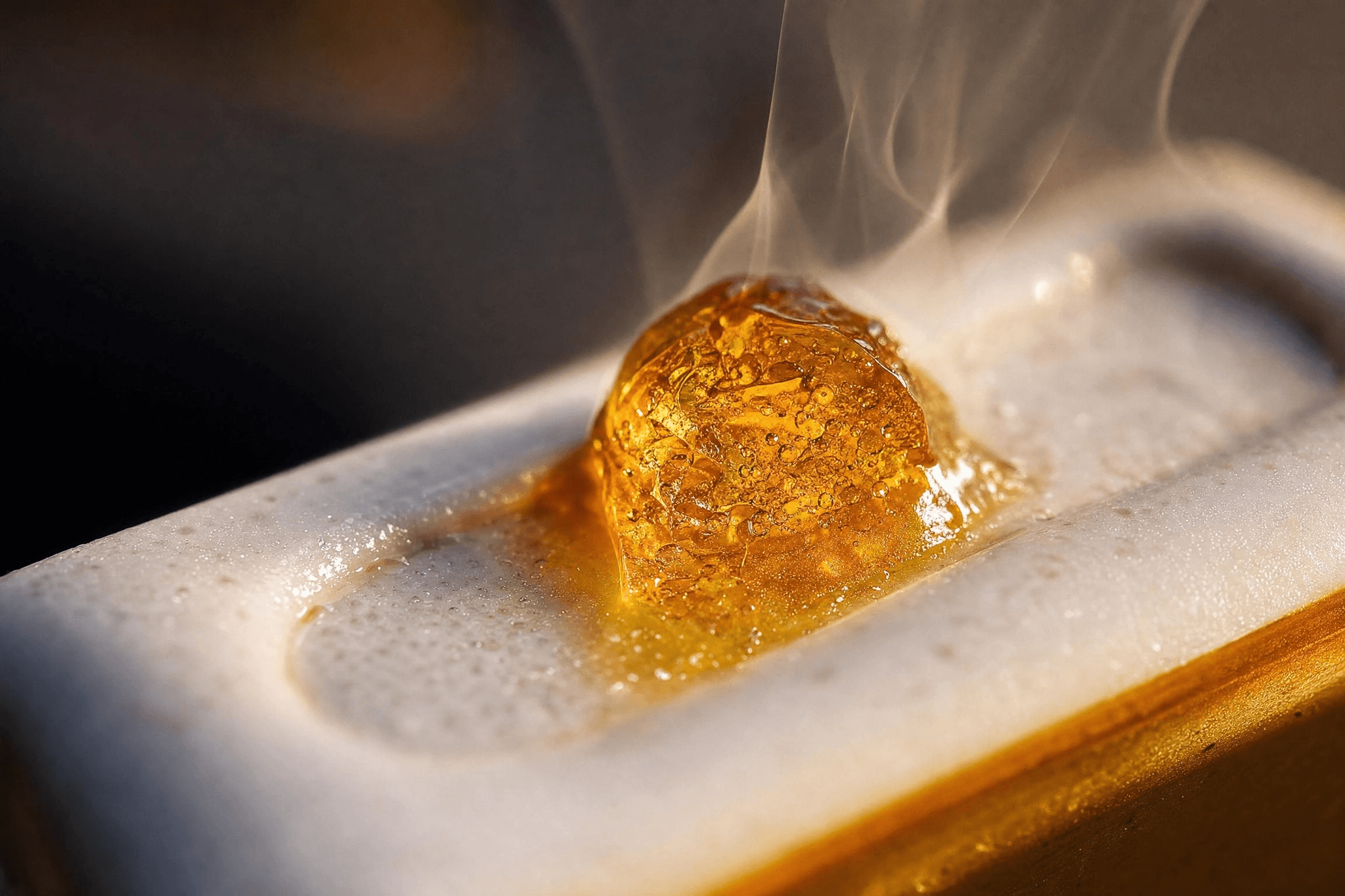 Nahaufnahme von schmelzendem goldenem Rosin-Konzentrat auf einem Keramik-Heizelement mit aufsteigendem Dampf.
