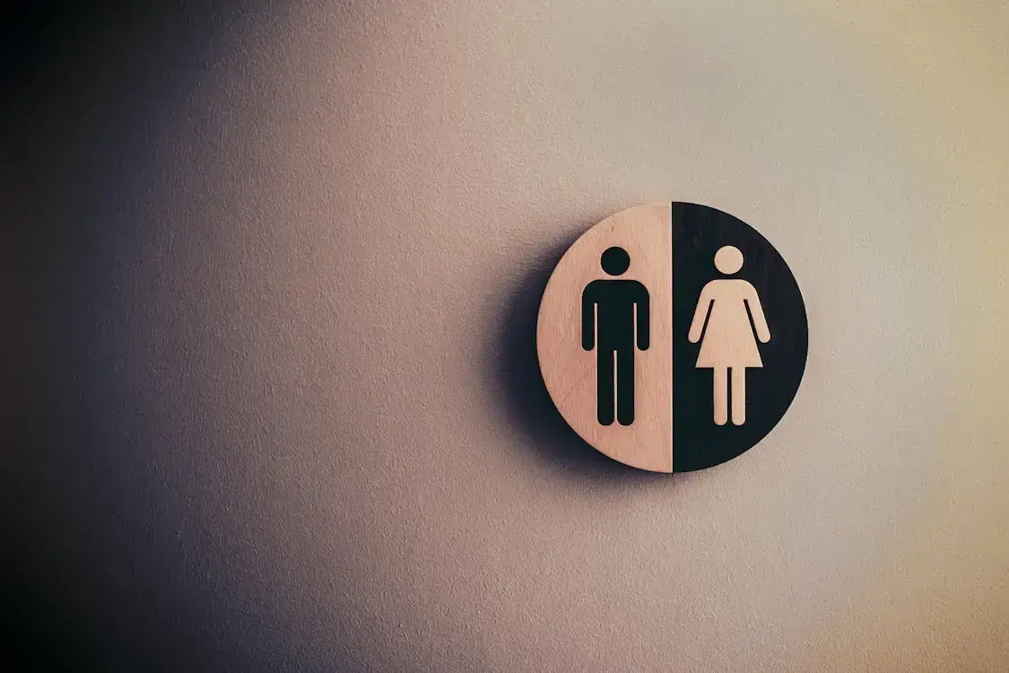 Rundes Schild mit geteilter Männer- und Frauensilhouette an heller Wand
