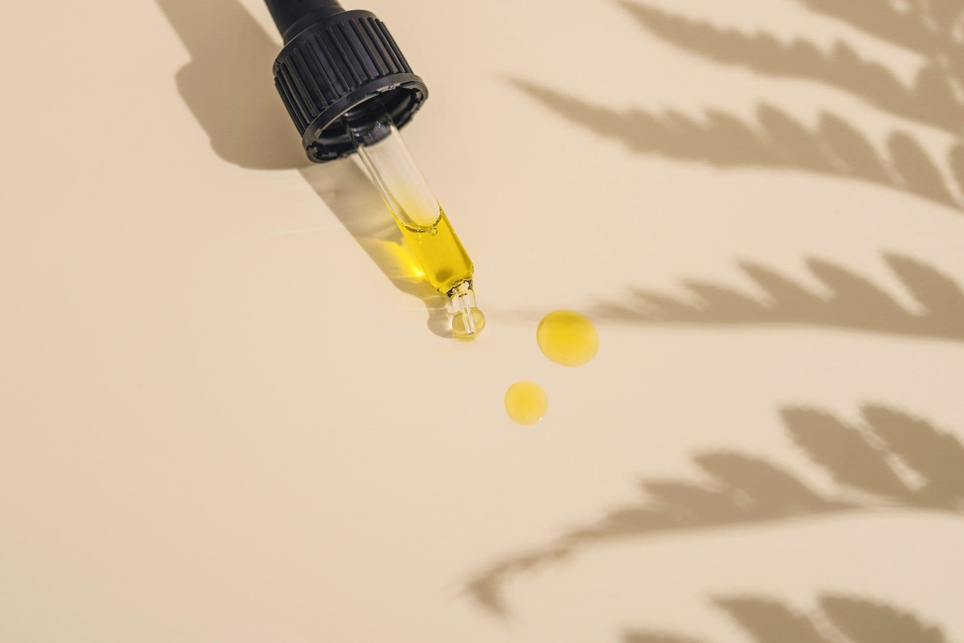 Glastropfer mit gelbem Öl und zwei Tropfen vor Pflanzenschatten