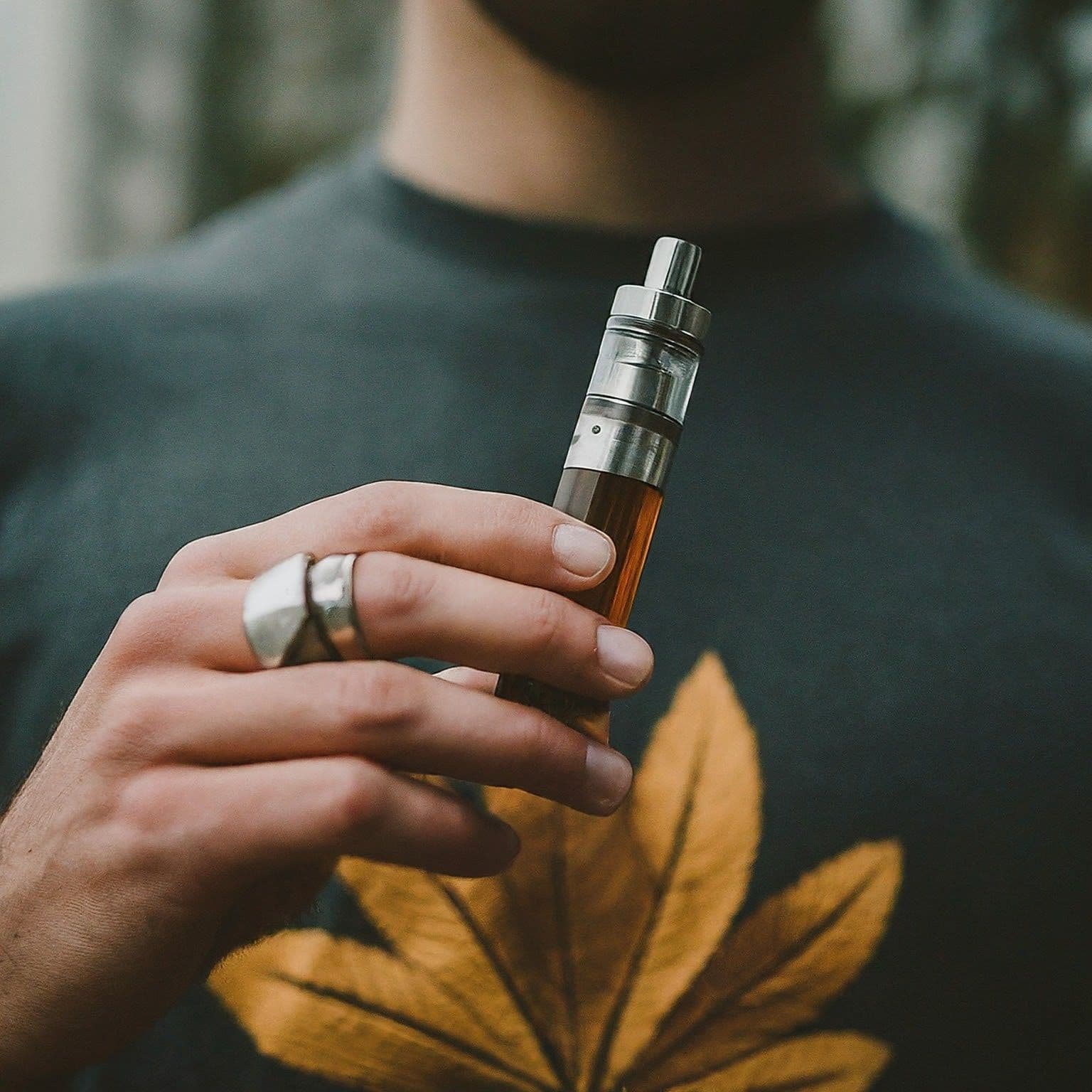 Hand mit Ring hält Vape-Pen mit bernsteinfarbener Flüssigkeit