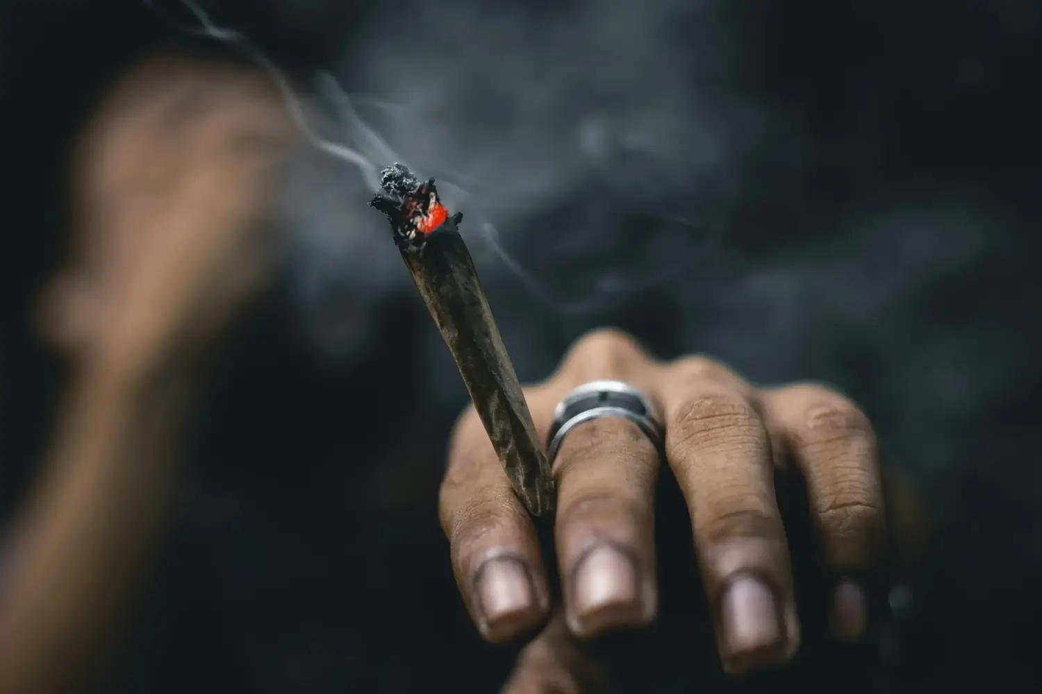 Hand hält brennenden Joint, Rauch steigt auf