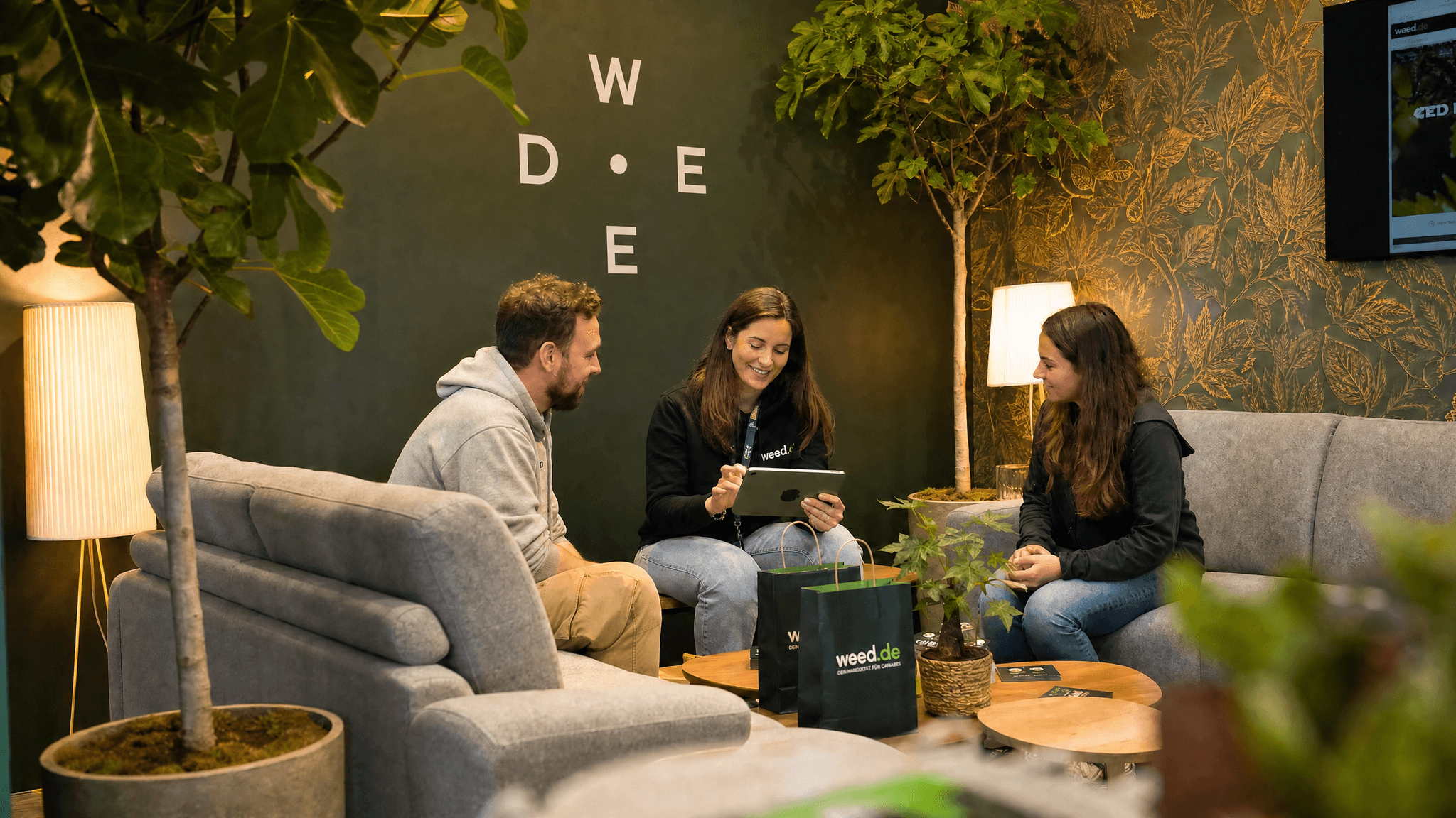 weed.de Team-Mitglied im Gespräch mit zwei Besuchern in der Chillout-Lounge am Messestand auf der MaryJane 2026