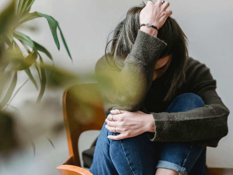 Sitzende Person umarmt die Knie, hält Kopf mit Hand