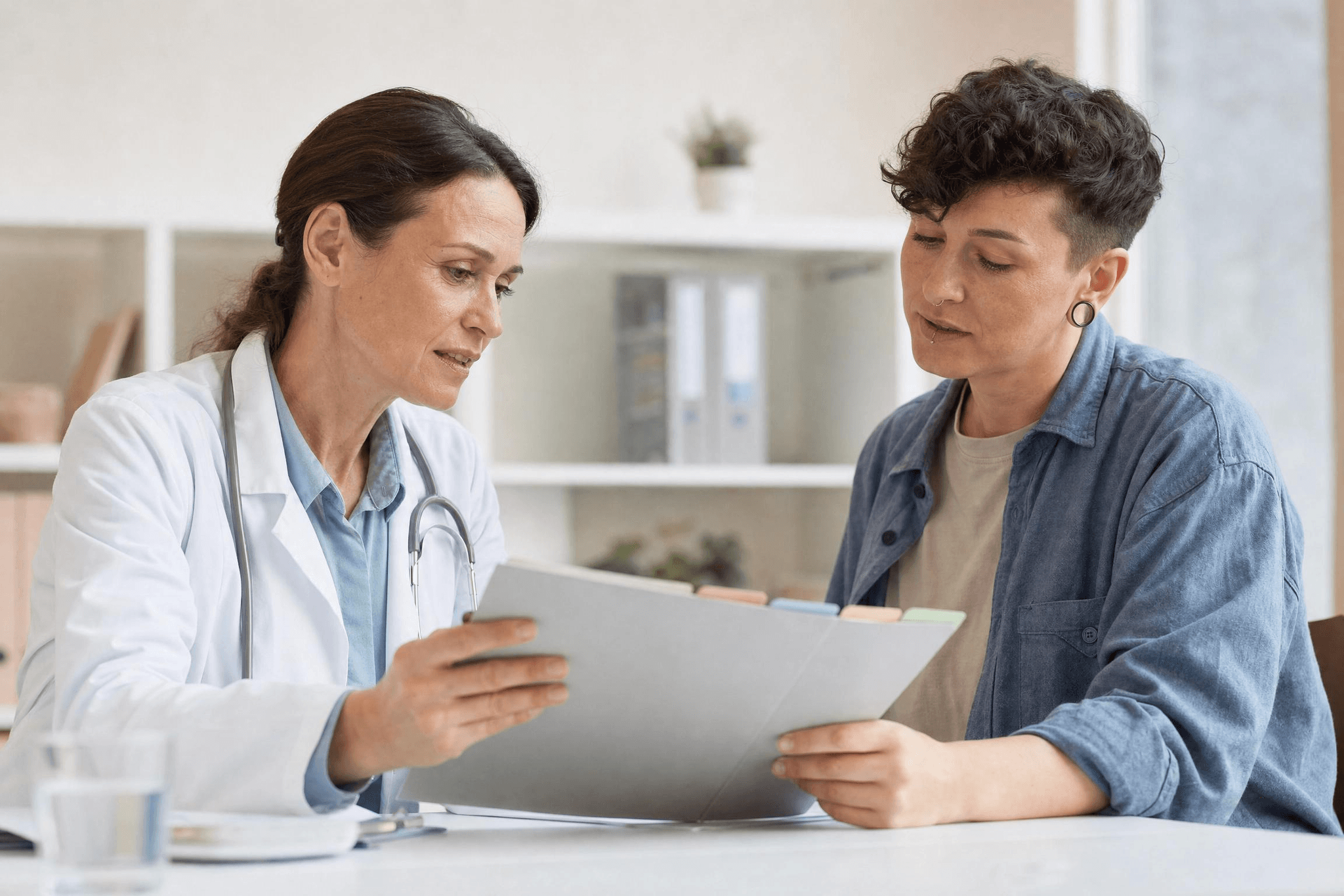 Ärztin und Patientin besprechen in einer Praxis eine Mappe mit Unterlagen zur medizinischen Einzelfallprüfung.