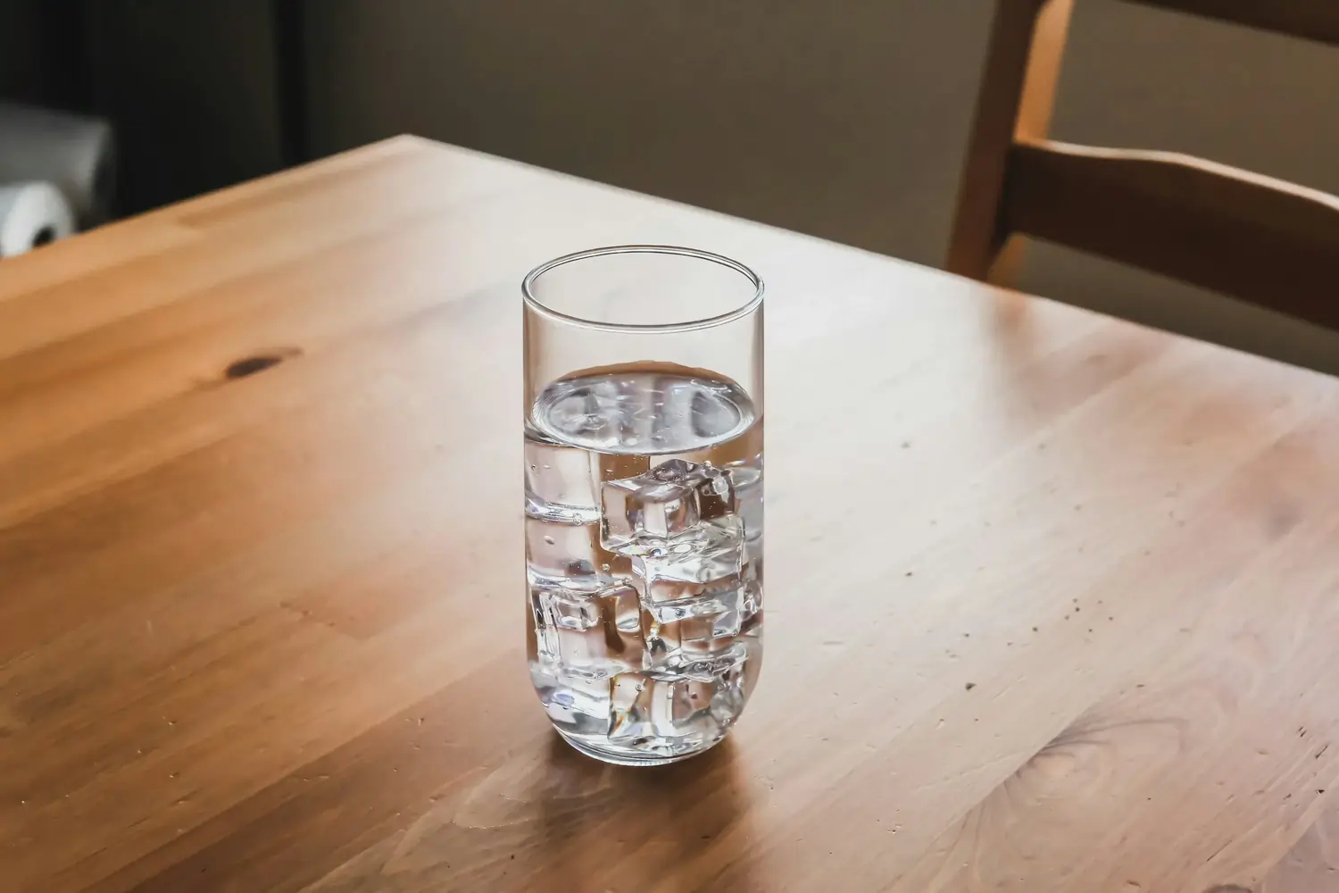 Hohes klares Glas mit Wasser und Eiswürfeln auf Holztisch