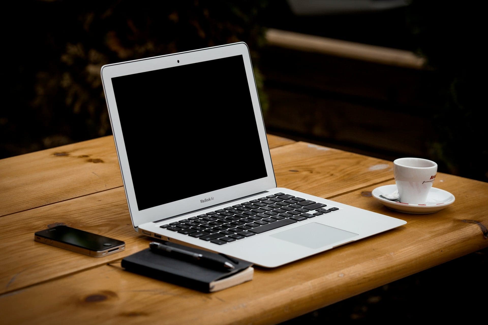 Silbernes Notebook mit schwarzem Bildschirm, Smartphone, Notizbuch und Espressotasse