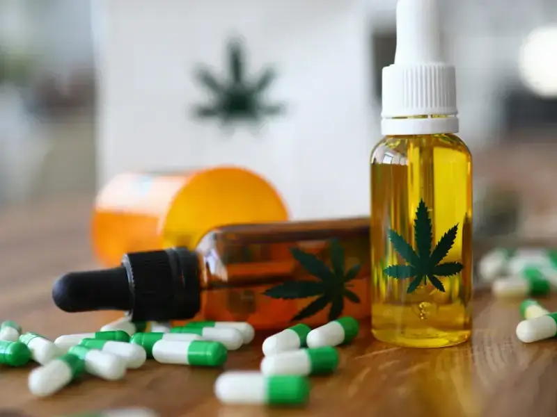 Flaschen mit CBD-Öl, Tropfer und grün-weißen Kapseln auf Holz
