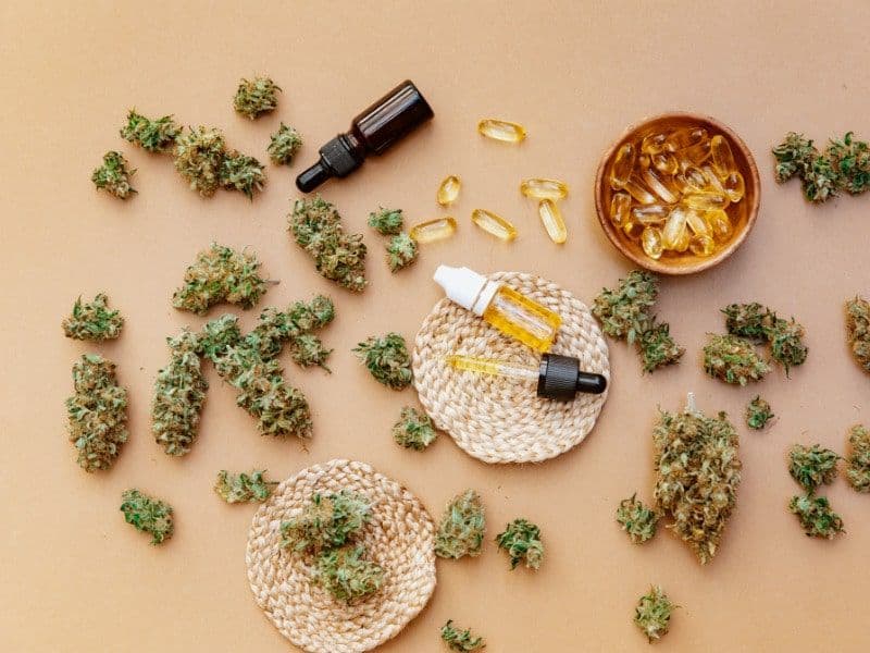 Cannabisblüten, Pipettenfläschchen mit Öl und Gelkapseln auf beigem Hintergrund