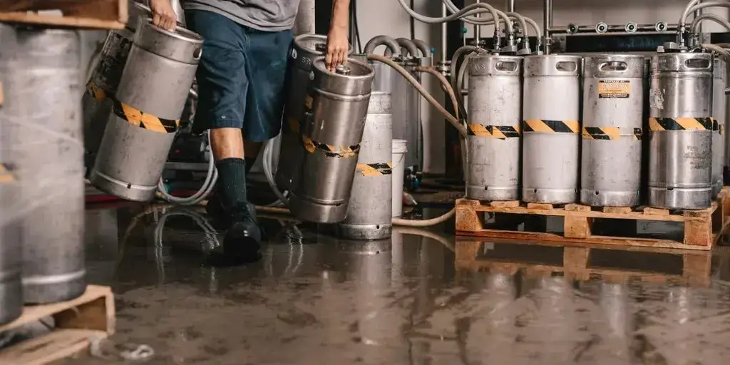 Person trägt Metallkegs über nassen Boden neben Zapfbehältern