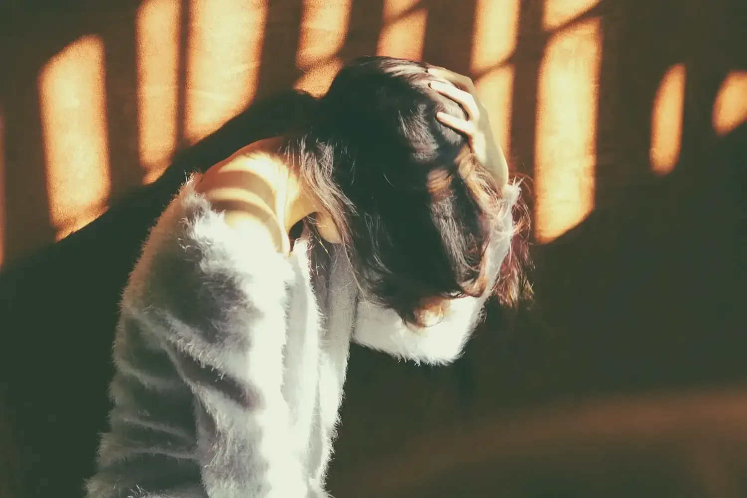Frau hält Kopf, Sonnenstreifen auf Haar und flauschigem Pullover