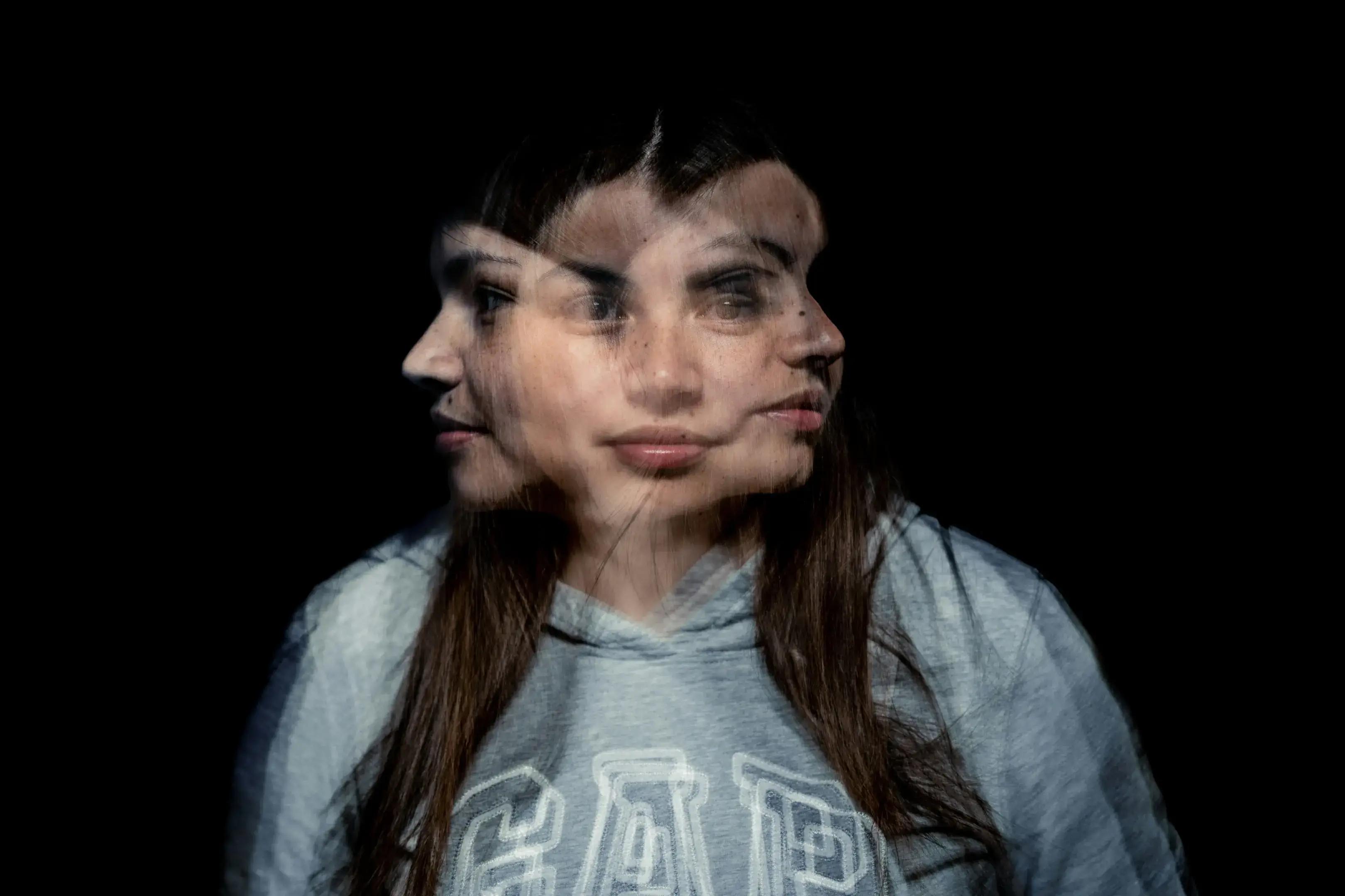 Frau im grauen Hoodie mit dreifacher Gesichtsüberlagerung vor schwarzem Hintergrund