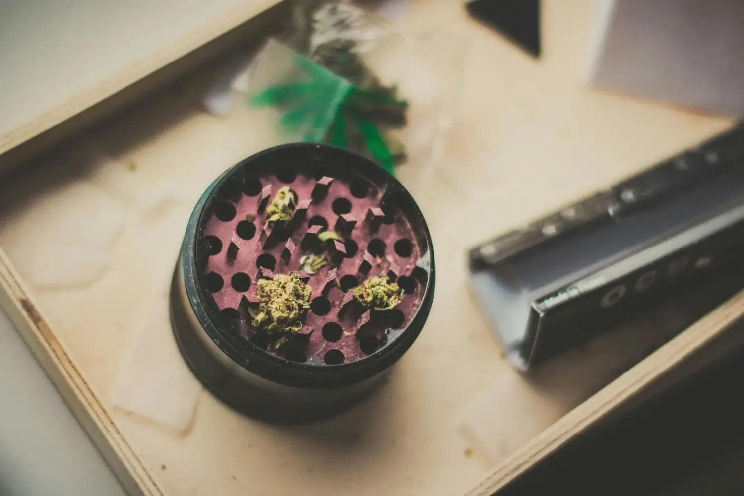Offener Grinder mit drei Cannabisblüten und lila Innenseite auf Holztablett