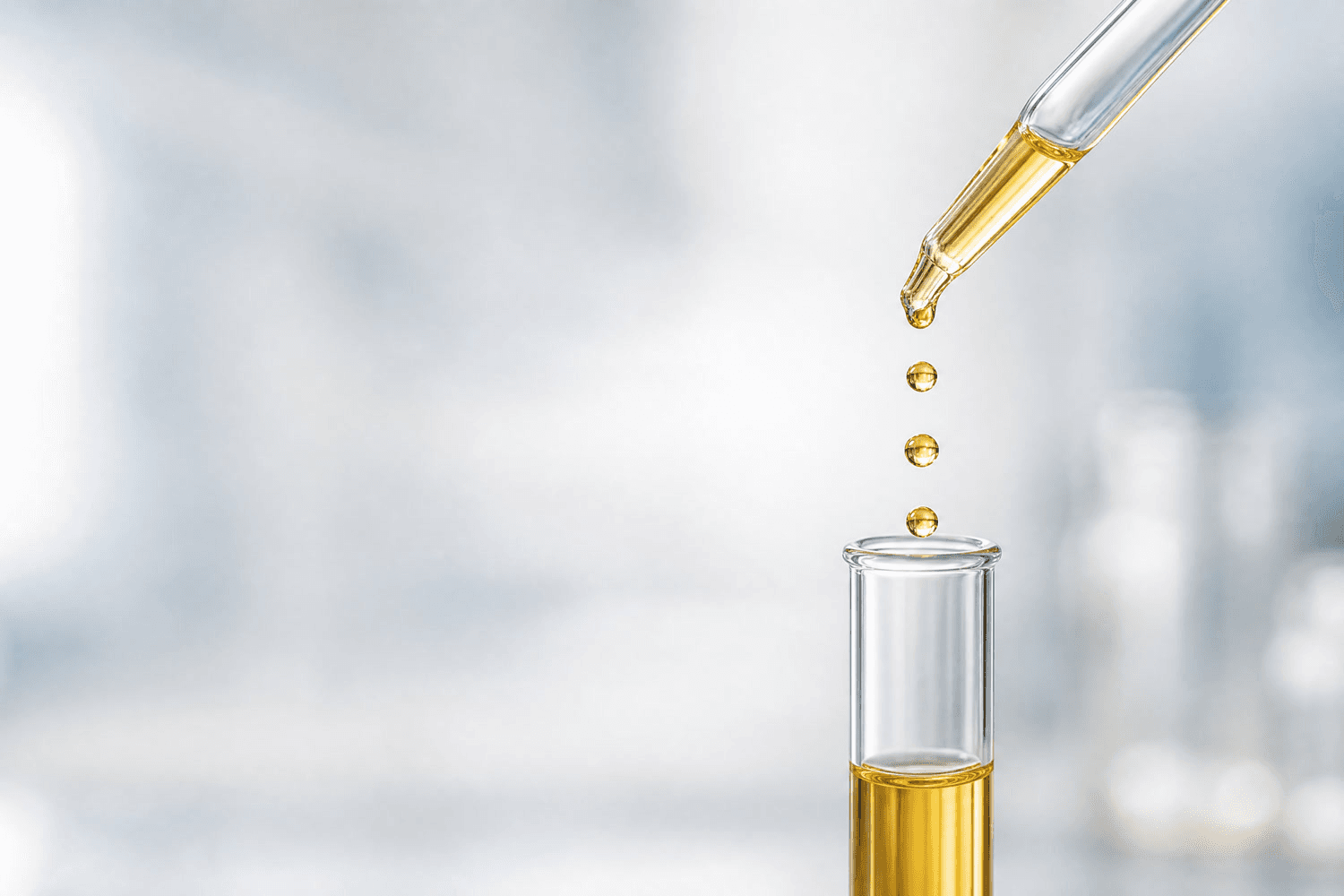 Transparente Glaspipette gibt goldfarbene Tropfen einer Dronabinol-Rezeptur in ein Reagenzglas mit öliger Lösung.