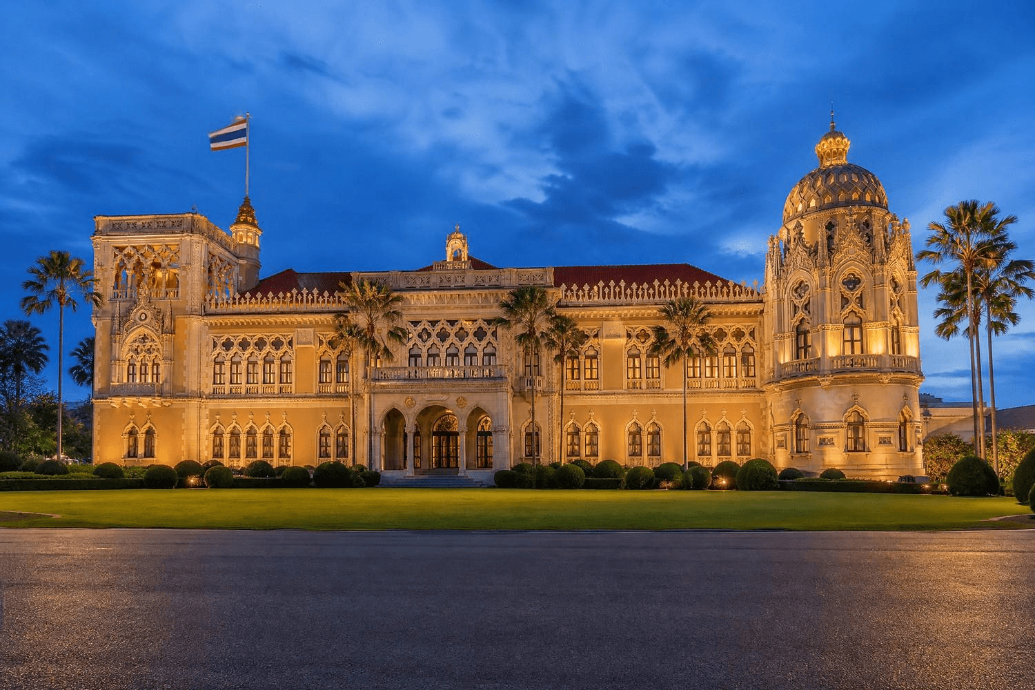 Das prachtvoll beleuchtete Regierungsgebäude Bangkoks (Government House) in der Abenddämmerung, mit der thailändischen Nationalflagge auf dem Dach und Palmen im Vordergrund – steht symbolisch für die politische Entscheidungsgewalt hinter Thailands Cannabis-Kehrtwende: Eine Ministerialverordnung öffnete 2022 den Markt, eine weitere schloss ihn 2025 wieder.
