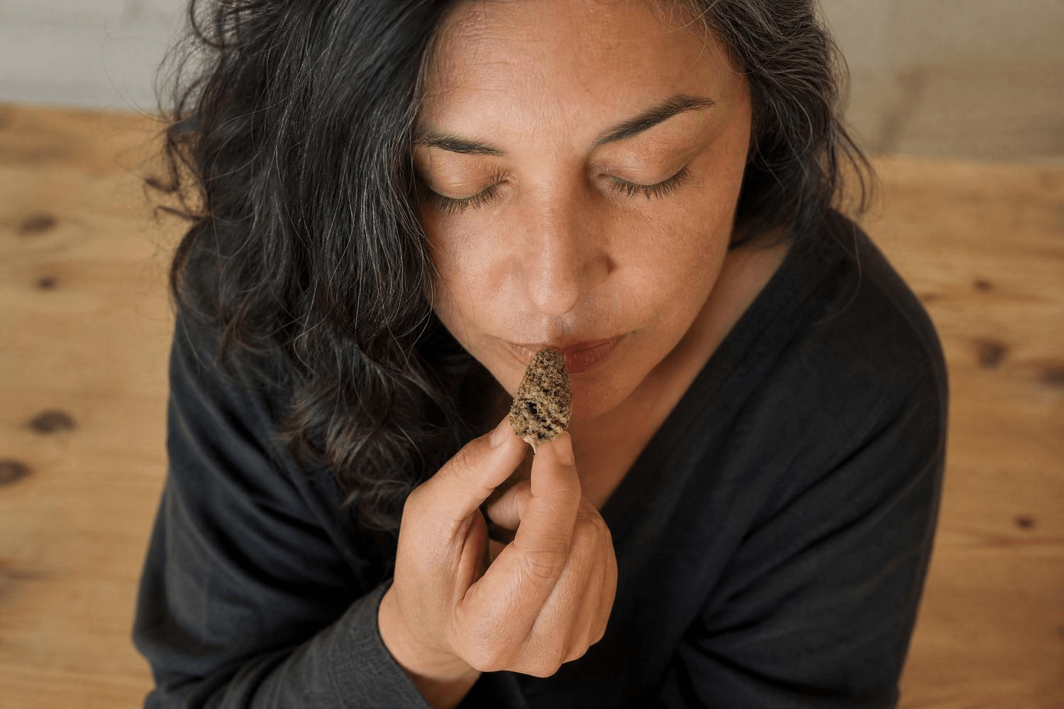Eine Frau mittleren Alters mit geschlossenen Augen hält eine getrocknete Cannabisblüte an die Nase und riecht daran – aufgenommen leicht von oben, ruhige, konzentrierte Stimmung.